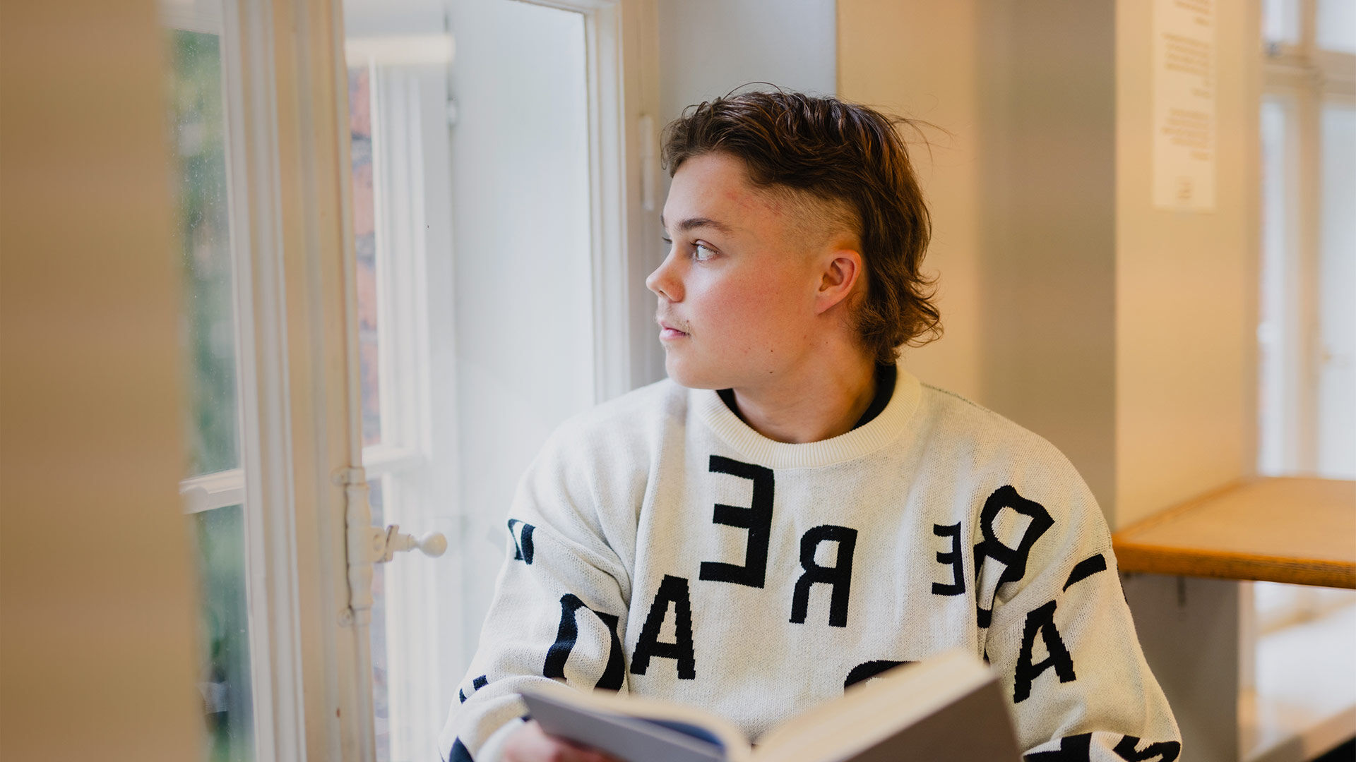 Nuori mies istuu ikkunan vieress&auml; lukemassa kirjaa